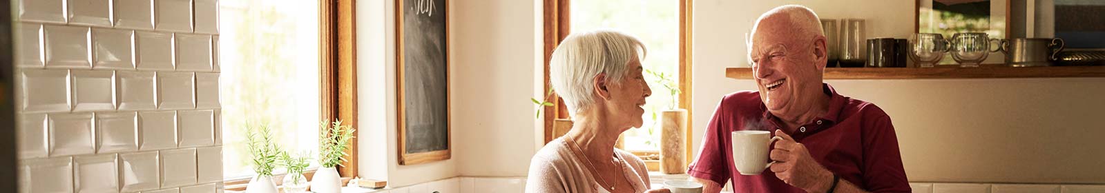 Mature couple laughing in kitchen while drinking coffee